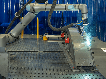 Industrial robotic arm welding a curved metal assembly with visible sparks